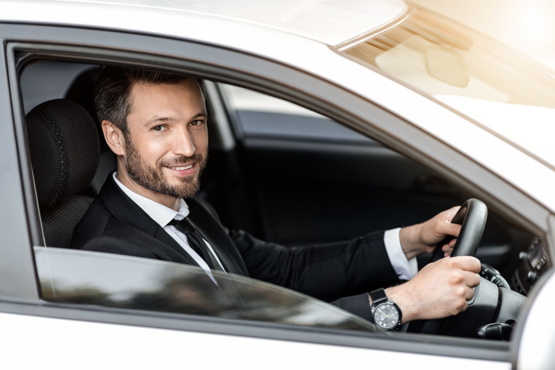 Fröhlicher erfolgreicher Geschäftsmann, der durch das Autofenster schaut